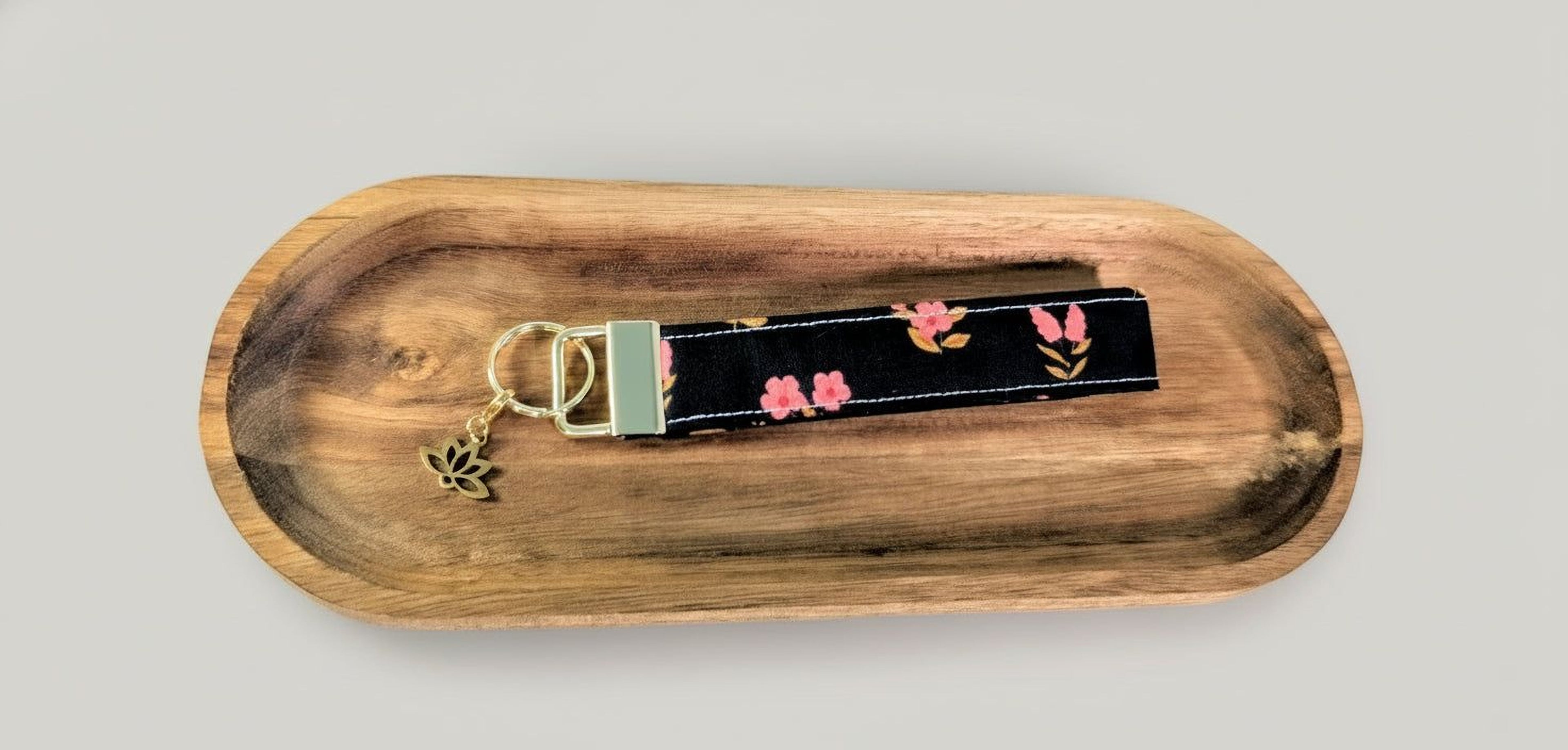 A black keychain with a floral pattern is placed on a wooden tray.