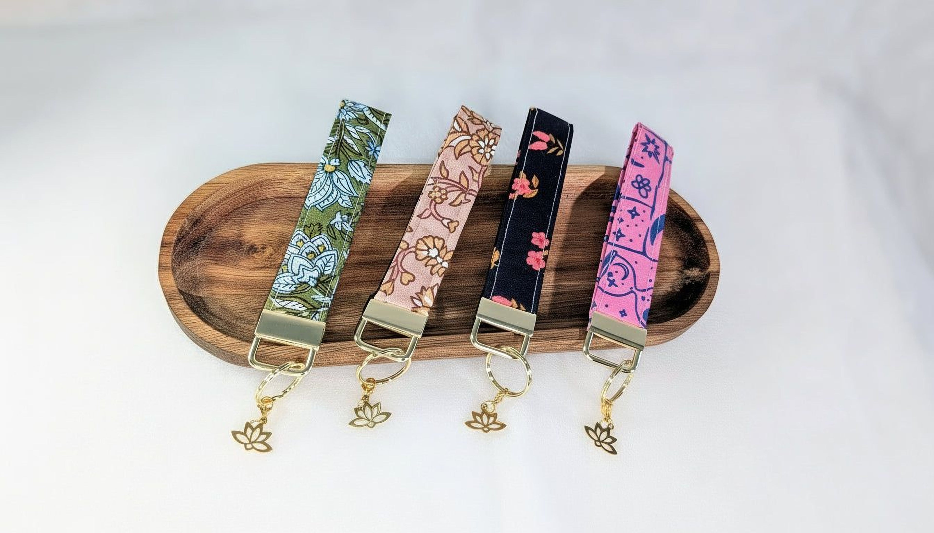 A wooden tray displaying four colorful keychains with different floral and geometric patterns.