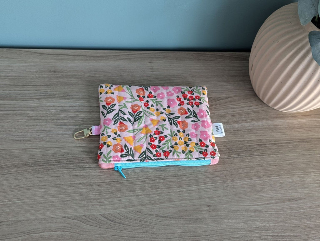 A colorful floral patterned pouch or wallet is placed on a wooden surface next to a vase.
