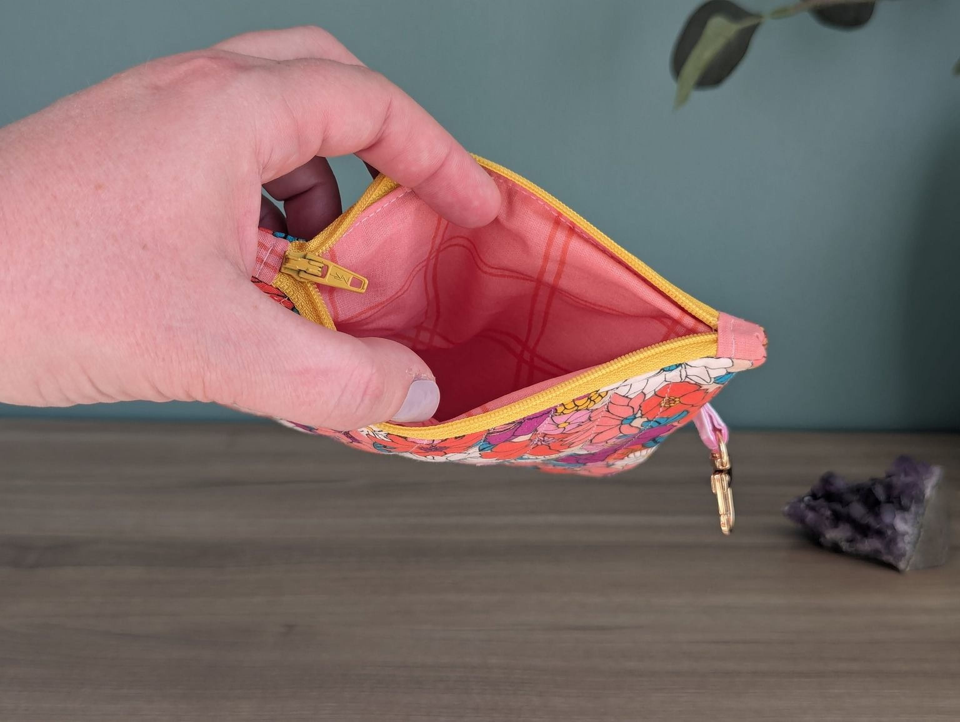 A hand is holding an open floral-patterned coin purse with a keychain attached, against a green background.
