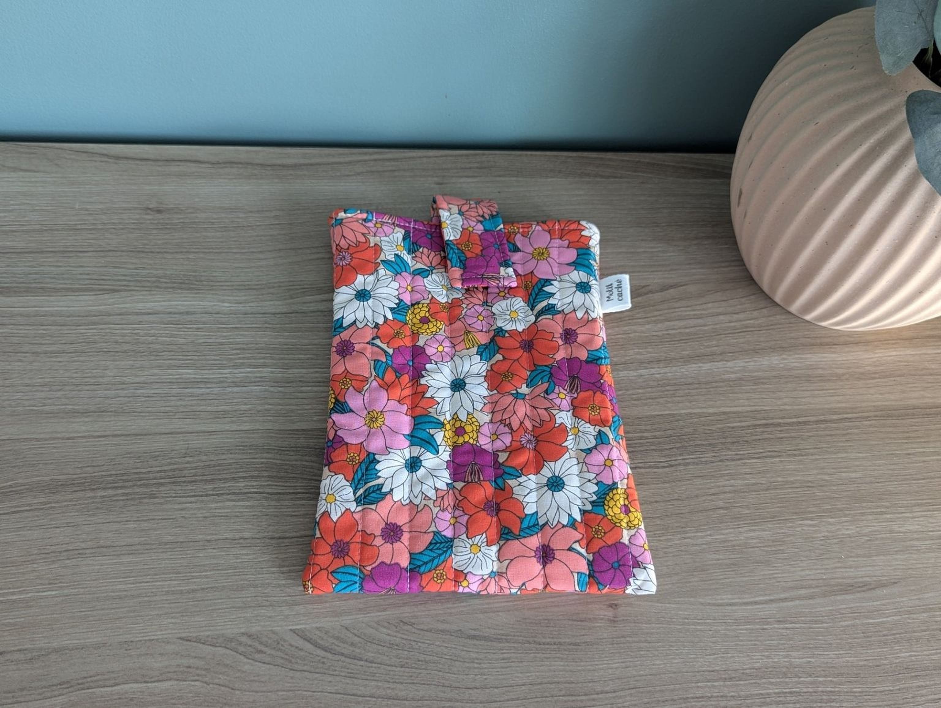 A colorful floral patterned bag or pouch is placed on a wooden surface next to a vase.
