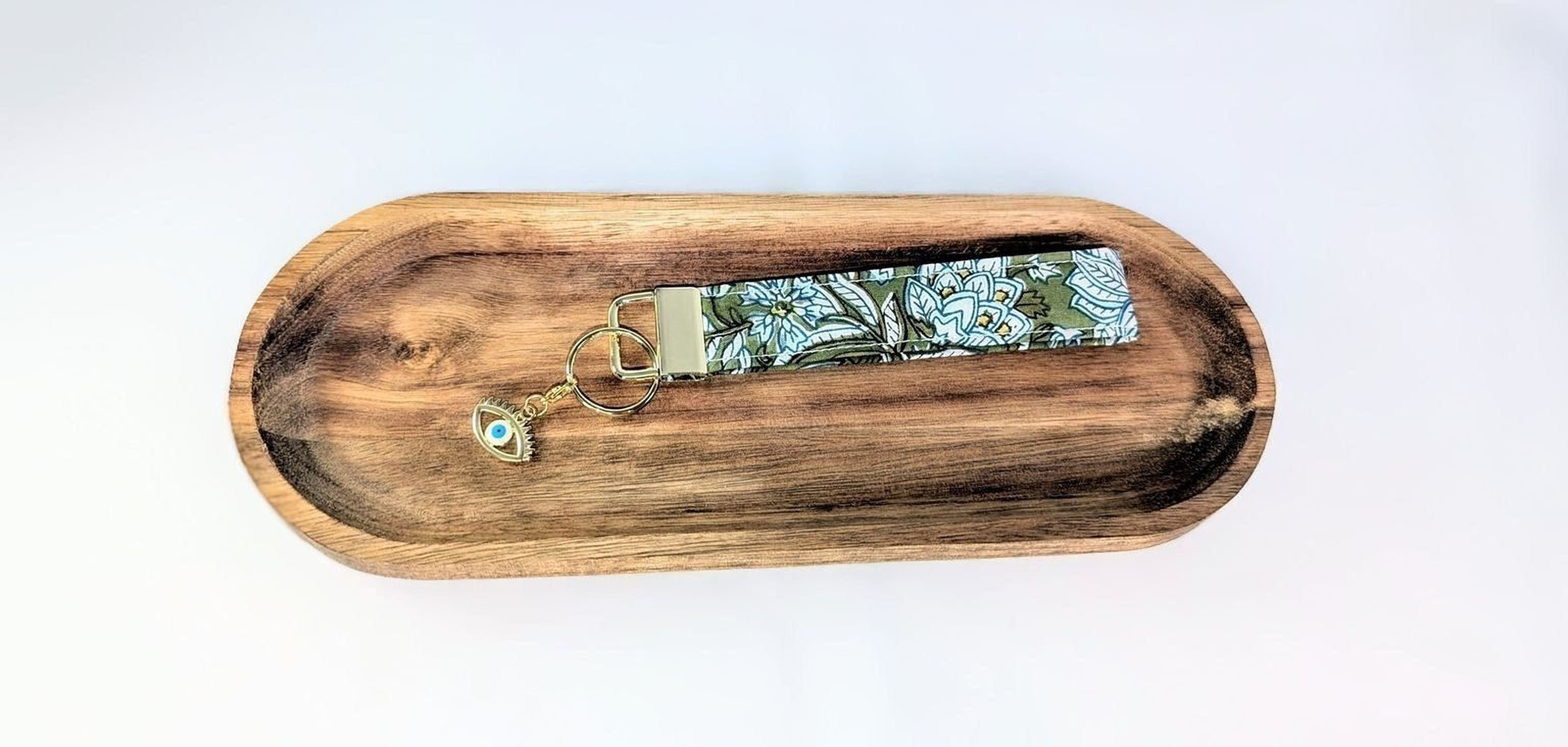 A wooden tray with a keychain featuring a floral pattern and a small eye charm.