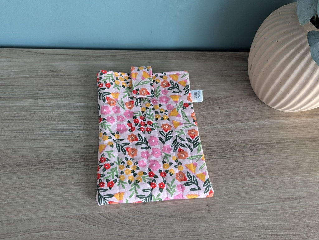 A colorful floral patterned bag or pouch is placed on a wooden surface next to a vase.