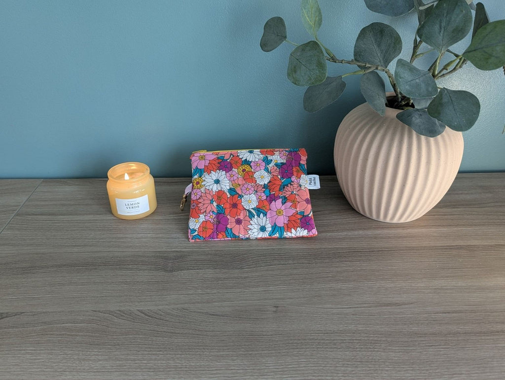 A wooden desk with a floral patterned bag, a candle, and a potted plant.