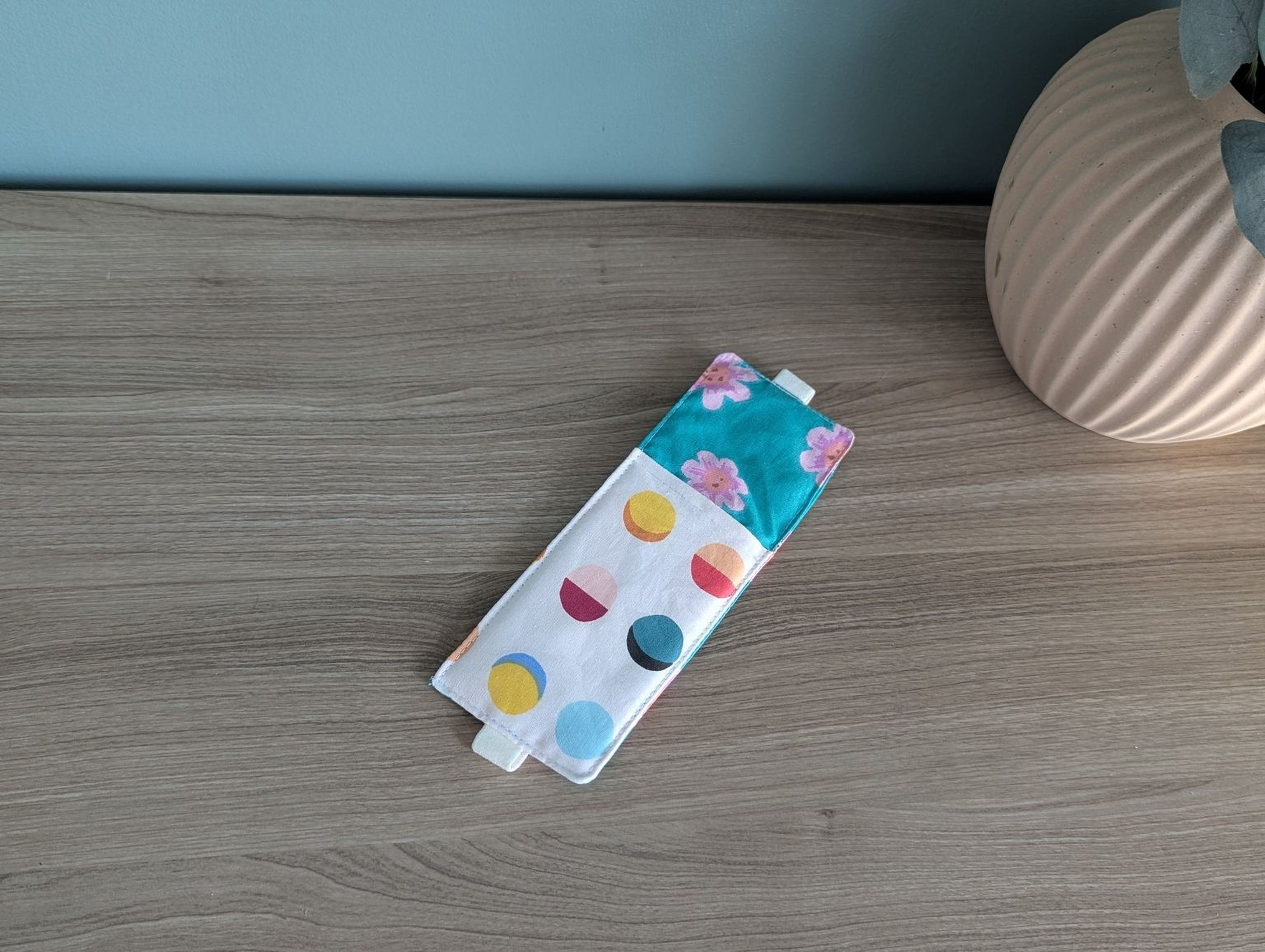 A colorful polka dot sleep mask is placed on a wooden surface next to a vase.