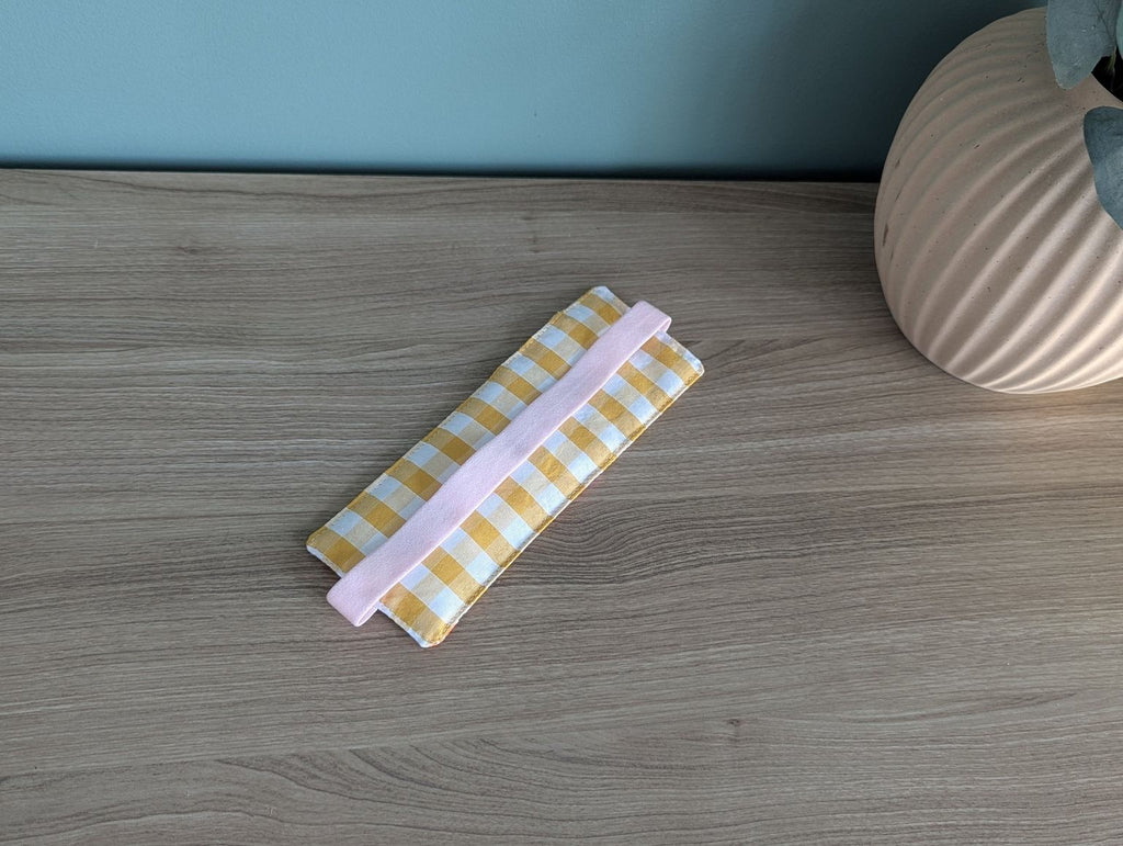 A checkered cloth with a pink handle is placed on a wooden surface, accompanied by a small vase and a plant.