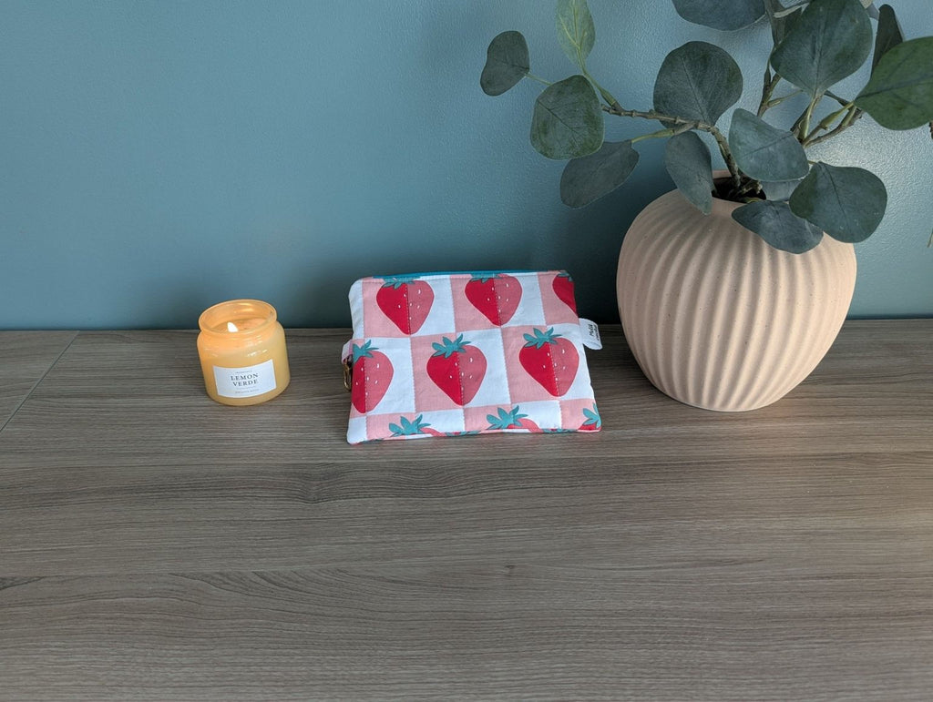 a wooden table with a candle, a small pouch with a strawberry pattern, and a potted plant.