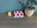 a wooden table with a candle, a small pouch with a strawberry pattern, and a potted plant.