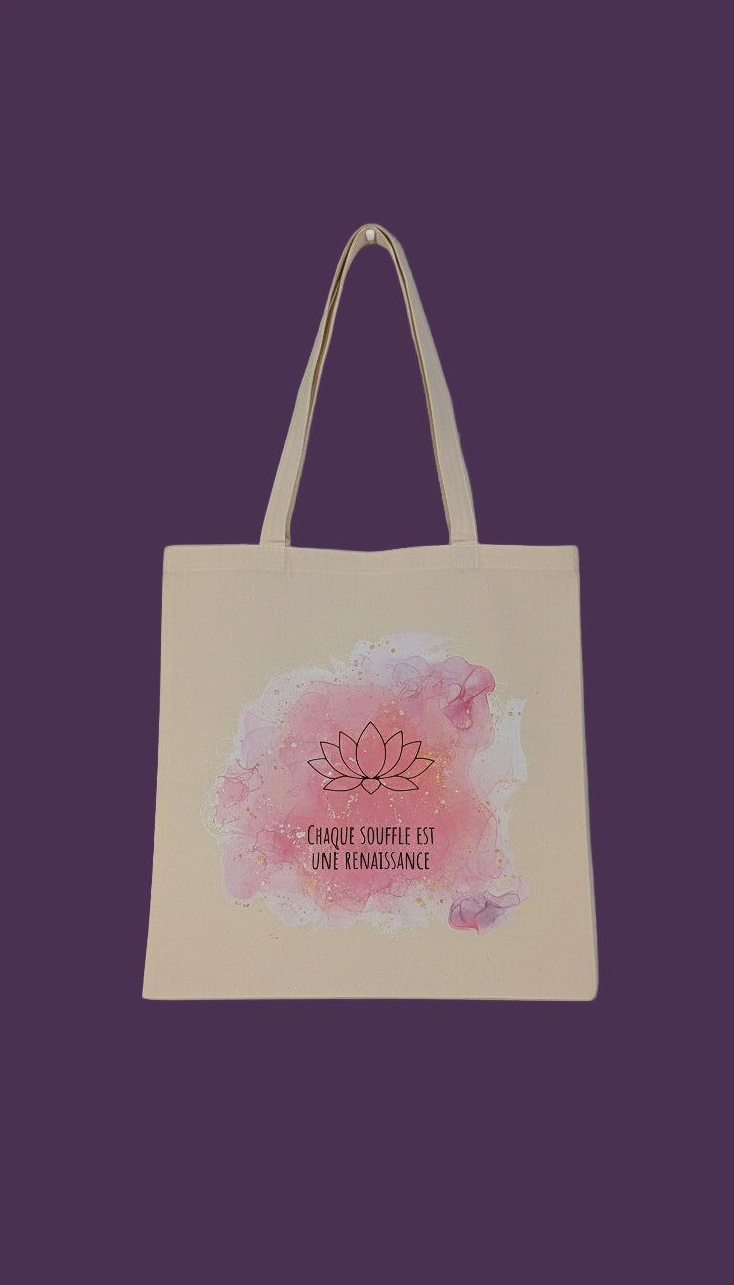 A beige tote bag with a watercolor design featuring a lotus flower and the text "Chaque souffle est une renaissance" (The lotus is a symbol of renaissance).