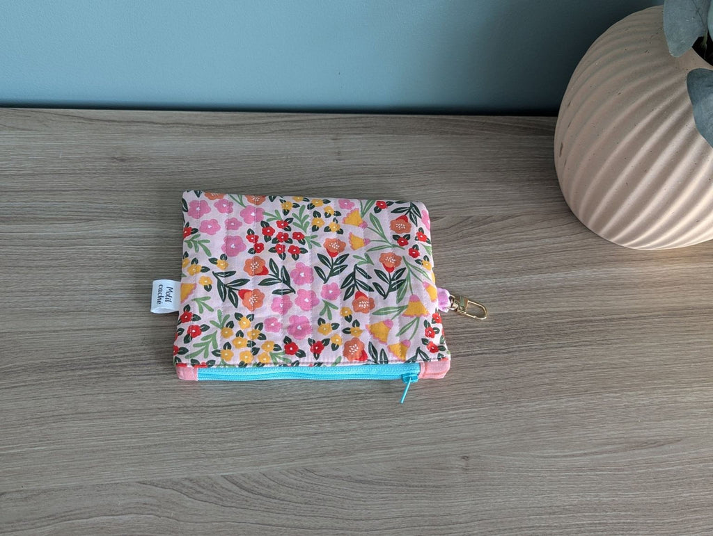 A colorful floral patterned pouch or wallet is placed on a wooden surface next to a vase.