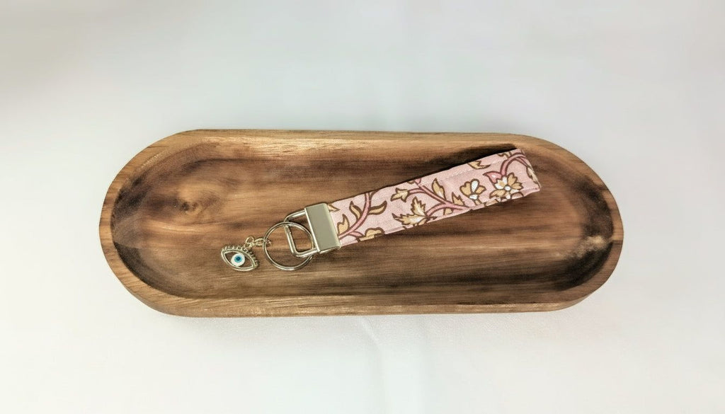 A wooden tray with a floral patterned keychain resting on it.